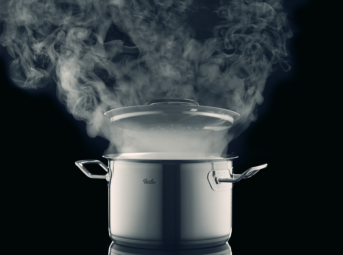 Steaming stainless steel pot on dark background
